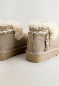 Tan samtige Knöchelstiefel mit weichen cremefarbenen Kunstfellumschlägen, dekorativen geflochtenen Akzenten und Gummisohlen mit strukturiertem Profil.