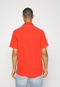 Rood T-shirt met korte mouwen gemaakt van lichtgewicht stof, met een puntige kraag en een rechte zoom, ontworpen met een ontspannen pasvorm.
