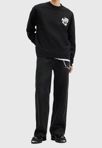 Black sweatshirt with white graphic print on the chest, paired with black wide-leg jeans. Shoes are black with a chunky sole.