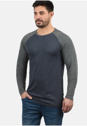 Chemise à manches longues à emmanchure raglan de couleur bleu foncé avec des manches grises. Fabriquée en tissu lisse, elle présente un col rond et une coupe décontractée.