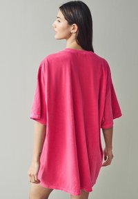 T-shirt oversize a maniche corte in tessuto rosa vivace con una consistenza morbida. Design semplice senza pattern o hardware notevoli.