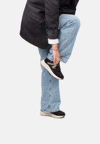 Baskets de sport noires avec tige en mesh et semelle beige, dotées de lacets contrastés et d'un motif texturé. Portées avec un jean blue et un blazer.