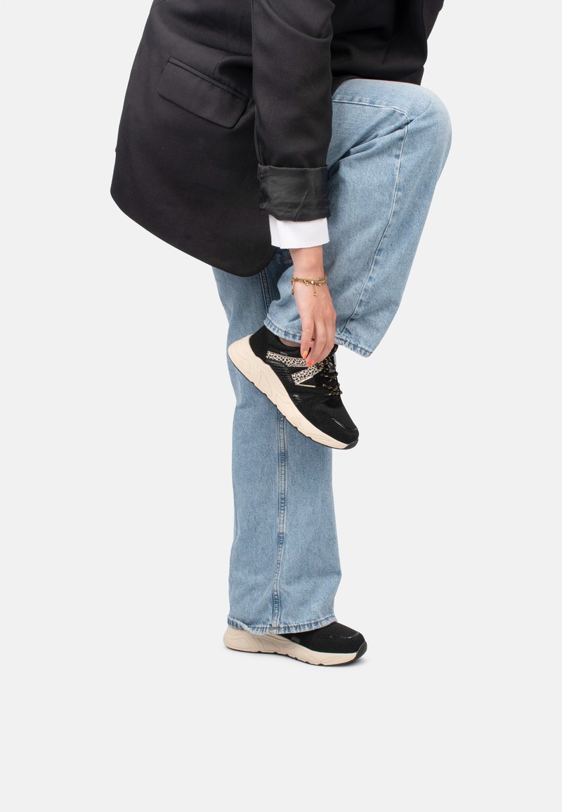 Baskets de sport noires avec tige en mesh et semelle beige, dotées de lacets contrastés et d'un motif texturé. Portées avec un jean blue et un blazer.