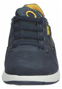 Zapatilla azul marino con parte superior de ante, acentos de malla, detalle de logo amarillo, seis ojales y suela de goma blanca.