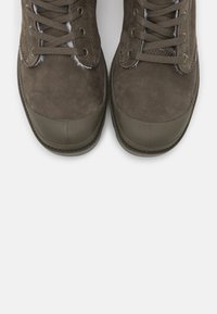 Olivgrüne Wildleder-Sneaker mit Gummikappe, runden Schnürsenkeln und gestickten Details an den Seiten. Glatte Textur, niedrig geschnittenes Design.