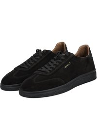 Black suede low-top sneakers with black laces, textured black sole, tan interior lining, and "GANT" logo in gold on the side.