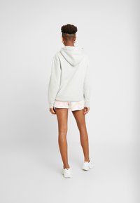 Šedá mikina s kapucí, doplněná o světle růžové šortky s technikou tie-dye. Texturovaná látka s volným střihem, nošena s bílými sportovními botami.