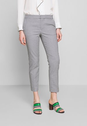 Pantaloni a scacchi bianco e nero con taglio slim, abbinati a sandali con tacco a blocco e punta aperta, caratterizzati da strisce verdi, blu scuro e bianche.