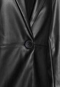 Blazer in pelle nera con texture liscia, risvolti affilati e una singola chiusura con bottone nero. Il tessuto presenta una leggera lucentezza.