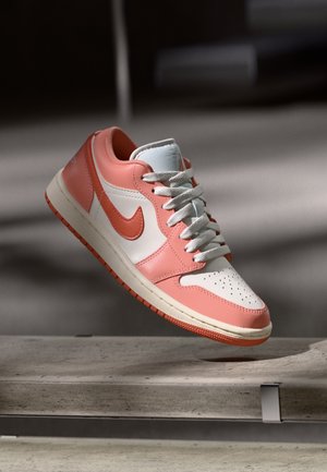 Zapatillas Nike que presentan una parte superior de cuero rosa con paneles blancos, una puntera perforada y acentos naranjas en el logo y la suela.