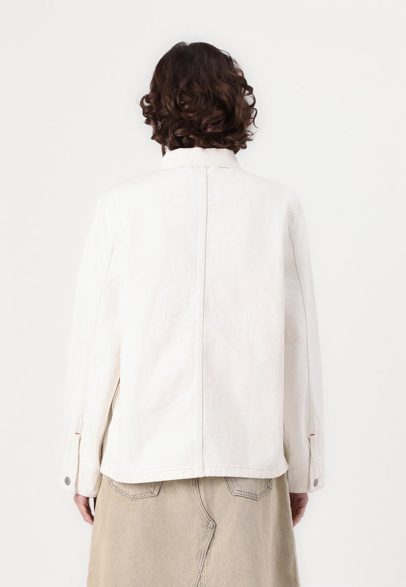 Veste en denim blanc avec un col structuré, des manches longues et des poignets boutonnés. Présente une couture arrière droite et un design minimaliste.