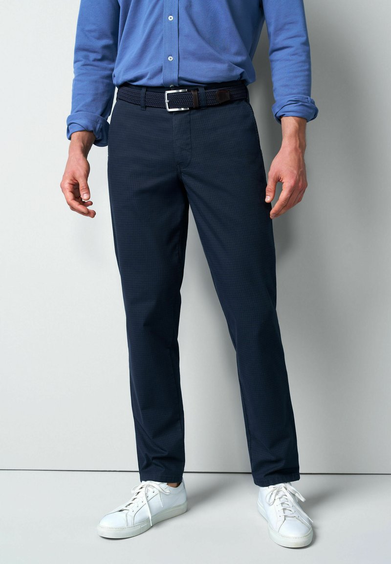 Marineblauwe, vlakke broeken met een subtiel ruitpatroon, gecombineerd met een blauwe button-down blouse en witte sneakers. Voorzien van een geweven riem.