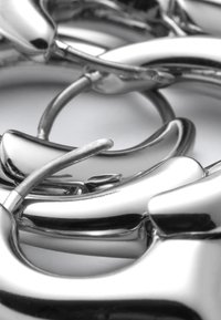 Gros plan sur des boucles d'oreilles créoles argentées brillantes avec fermoirs à charnière, disposées sur une surface blanche.