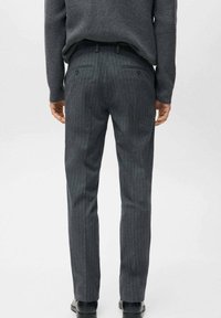 Pantaloni grigi a righe con vestibilità su misura, caratterizzati da due tasche posteriori e una superficie liscia. Indossati con un maglione scuro a maglia.