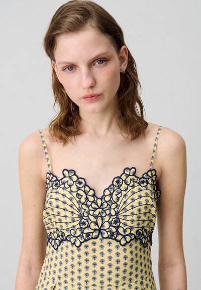 Abito giallo con ricami floreali blu navy. Presenta spalline sottili e scollatura a V. Tessuto morbido con una texture delicata, messa in risalto da motivi intricati.