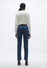 Heledates toonides kootud kampsun, sobitatud tumeliste siniste kõrge vöökohaga teksapükstega. Teksadel on klassikaline viiepiste taskute disain ja peened õmbluse detailid.