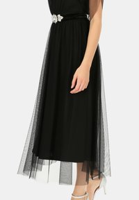 Czarna sukienka z dopasowanym gorsetem, przezroczystą tkaniną z tiulu oraz szerokim welurowym paskiem ozdobionym dekoracyjną srebrną klamrą.