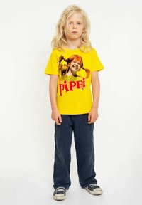 Yellow short-sleeve t-shirt featuring a printed graphic of a character with red hair and pigtails, paired with dark blue pants and sneakers.
