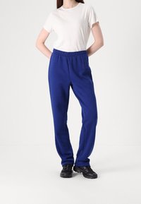 Blå sweatpants i mjukt tyg med elastisk midja, raka ben med sömmar på sidorna, i kombination med en enkel vit t-shirt.