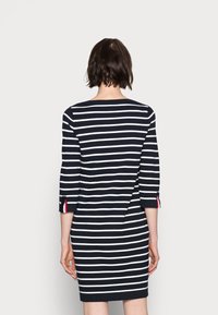 Robe à rayures bleu marine et blanches avec manches trois-quarts, fente au dos et accents rouges aux ouvertures des manches. Tissu doux et texturé.