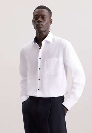 Witte button-up blouse met een slim fit, zwarte knopen en een marineblauwe geblokte kraag. Heeft een enkele borstzak en lange mouwen.