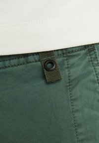 Gröna bomullsbukser med en strukturerad textil, synliga sömmar och en vävd ögla med en svart ögla fäst.