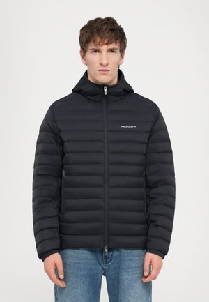 Veste en duvet noire avec capuche, présentant une texture matelassée horizontale, une fermeture éclair à l'avant et un détail de logo sur la poitrine. Coupe standard.