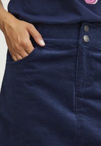 Gonna in corduroy blu navy con righe verticali evidenti, chiusura con due bottoni in vita e tasca laterale. Texture liscia con leggero lucido.