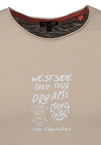 Camiseta beige con texto impreso en blanco que dice "WESTSIDE TOMA TUS SUEÑOS", "DE WEST LA", "NACIDO ASÍ" y "low rider oldies."