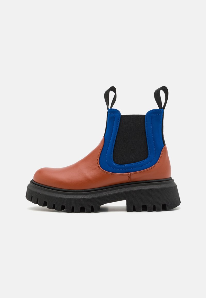Bottine Chelsea avec devant en cuir marron, panneaux latéraux extensibles bleu et noir, semelle épaisse noire à crampons, et languettes noires sur le dessus.