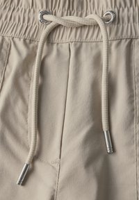 Beige shorts met een elastische tailleband, voorzien van een trekkoord met zilveren metalen punten en een gladde, lichte stofstructuur.
