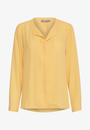 Långärmad gul blus i lätt tyg, med en kraglös halsringning, framplacket och en något böjd nederkant.