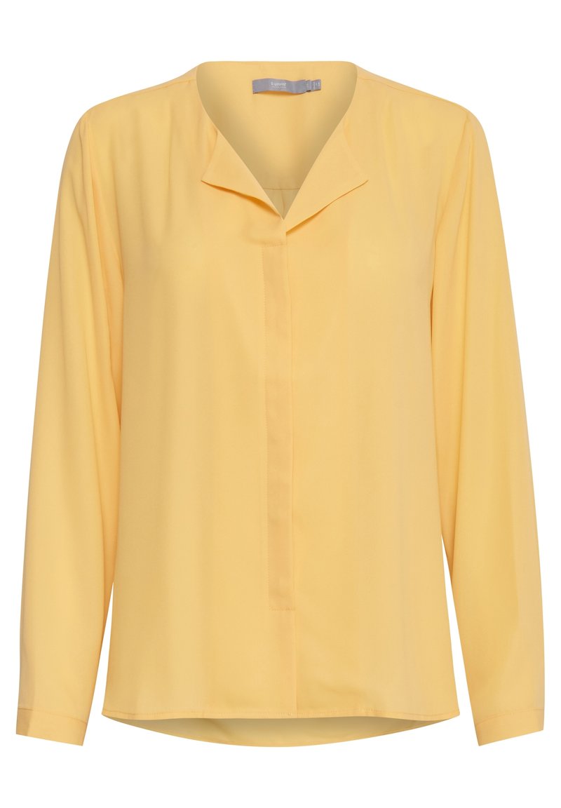 Blusa gialla a maniche lunghe in tessuto leggero, con scollatura senza colletto, patta frontale e orlo leggermente curvato.