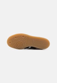 Semelle de chaussure en caoutchouc de couleur gomme avec un motif texturé. Présente des points de grip circulaires et ovales, avec une section supérieure noire visible.