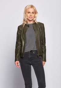 Olivgrön läderjacka med en figursydd design, smal silhuett, ståkrage och dragkedjefickor. Kombinerad med en grå topp och svarta jeans.