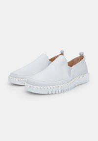 Balti slip-on batai, pagaminti iš lygios odos, su elastingomis šoninėmis dalimis, tekstūruota balta guminė padu ir minimaliais siuvinėjimo akcentais.