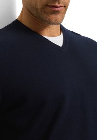 Marineblauwe V-hals trui van gladgebreide stof, met een aansluitend model en een subtiele textuur. Gelaagd over een wit overhemd.