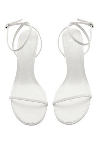 Białe sandały na płaskiej podeszwie z paskami, o minimalistycznym designie i smukłej sylwetce, z regulowanym paskiem na kostkę. Gładka faktura na całej powierzchni.