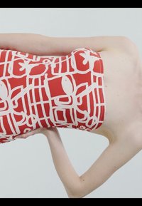 Robe rouge bustier avec des motifs géométriques abstraits blancs et floraux portée par une personne avec un bras plié derrière le dos.