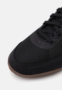Czarne buty sportowe z siateczkową cholewką, zamszowymi akcentami, teksturowaną gumową podeszwą i kontrastującymi sznurówkami.