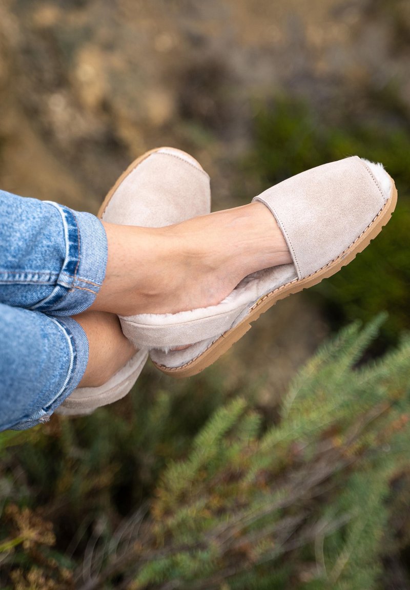Chaussures à enfiler beige clair en daim, dotées d'une doublure intérieure douce, d'une semelle plate et d'un bout arrondi, sur un fond naturel.