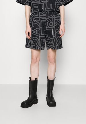 Sorte shorts med hvide geometriske tekstmønstre og en matchende skjorte, parret med knælange sorte læderstøvler med en tyk sål.