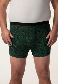 Boxer da uomo con motivo floreale verde e vita nera, caratterizzati da una vestibilità aderente e una texture morbida, esposti su uno sfondo neutro.