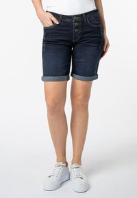 Denim shorts in een donkere wassingen met opgerolde mouwen, vijf zakken en een knoopsluiting. Gecombineerd met witte platform sneakers.