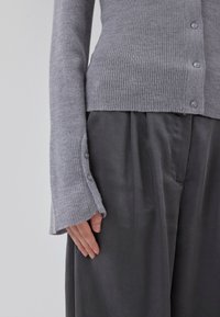 Gray ribbed cardigan with buttons, featuring long sleeves with wide openings. Gray textured pants partially visible beneath.