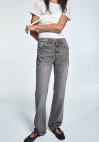 Šedé džíny s vysokým pasem a uvolněným střihem, mají pět kapes a denimovou strukturu. Nosí se s bílým upnutým tričkem a černými balerínami.