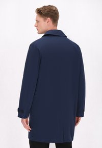 Mørkeblå trenchcoat lavet af letvægtsstof, med en klassisk krave, lange ærmer med knapdetaljer og en mellemlang design.