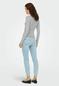 Šedý top s dlhým rukávom a rebrovanou textúrou, v kombinácii so svetlomodrými slim-fit džínami. Čierne balerínky s mašľou. Pohľad zozadu.