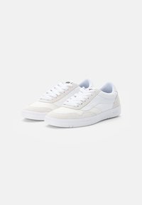 White canvas sneakers featuring a textured side panel, rounded toe, flat laces, and a white rubber sole with "VANS" branding on the heel.