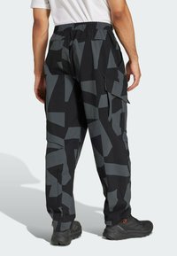 Zwarte cargobroek met grote grijze geometrische patronen. Heeft een elastische tailleband en zijzakken. Draagt met zwarte gestructureerde schoenen.